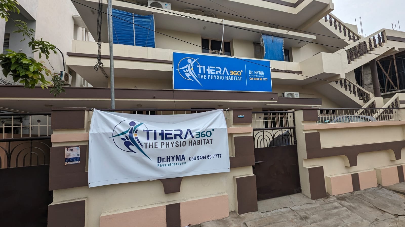 Daytime street view of the Thera360 (The Physio Habitat) clinic in Ramanayyapeta, Kakinada, with Dr. Hyma physiotherapy banners on the building